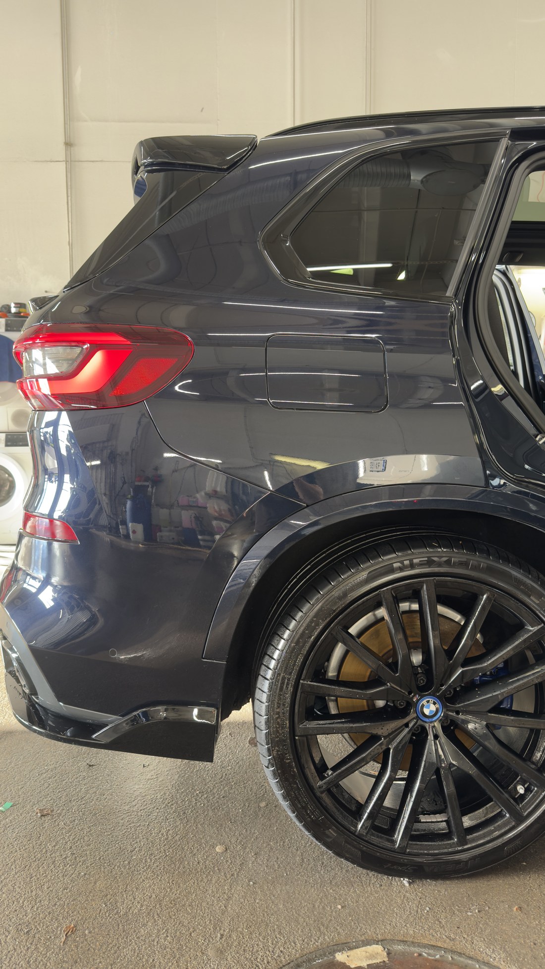 Musta BMW X5 tagaosa ja tagatiib pärast hooldust, pind peegeldab töökoja valgust